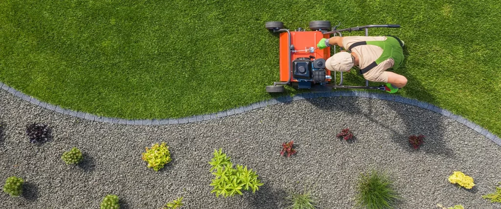 Lawn care professional mowing grass with a red push mower, maintaining a well-kept yard