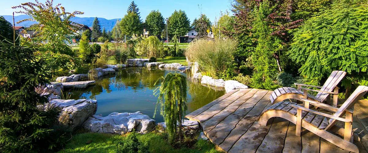 Beautiful backyard pond with lush landscaping and wooden deck seating area, perfect for outdoor relaxation and garden aesthetics.