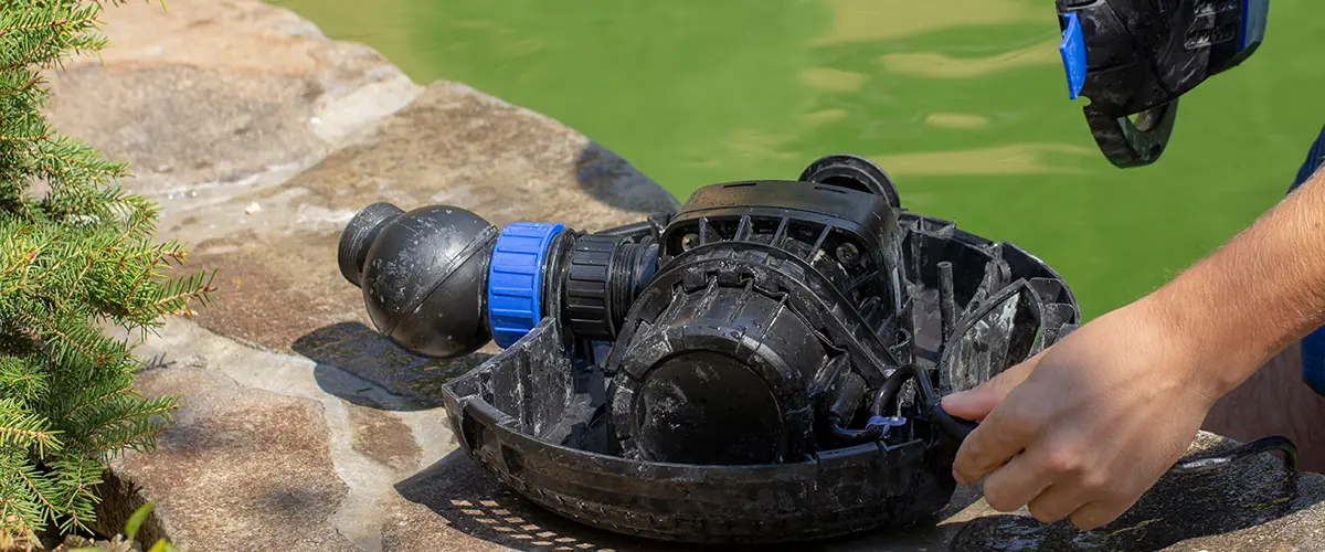 Hands repairing a pond pump near a garden water feature, essential maintenance for a healthy backyard koi pond or water garden system.