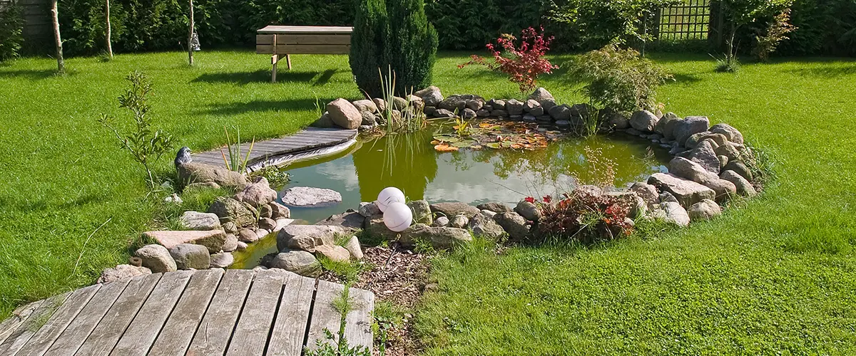 Natural-style garden pond with wooden bridge and rock border