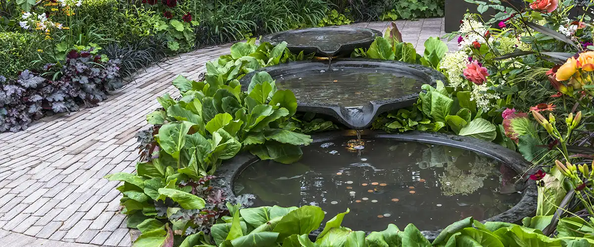 Garden pond with tiered bowl water feature surrounded by plants