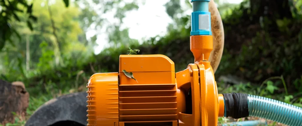  koi pond maintenance florida orange industrial water pump with blue components positioned on a concrete base surrounded by lush green outdoor foliage demonstrating professional equipment setup
