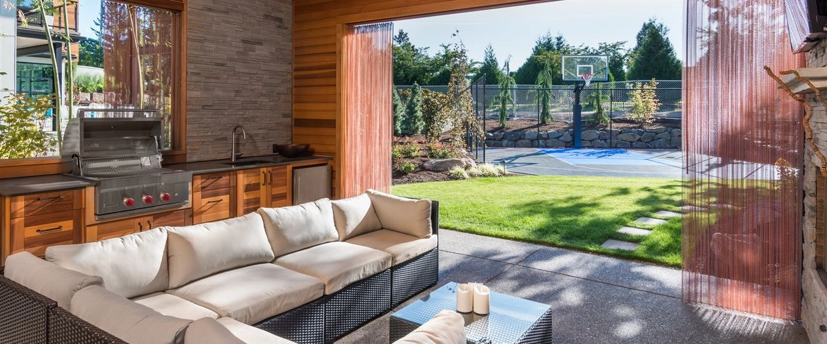 Luxury outdoor living area featuring a built-in outdoor kitchen, comfortable L-shaped patio sofa, and a paver patio extending to a backyard basketball court