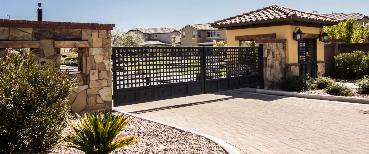 a modern double metal entry gate with a walk-through structure, paver driveway, and a flagstone wall