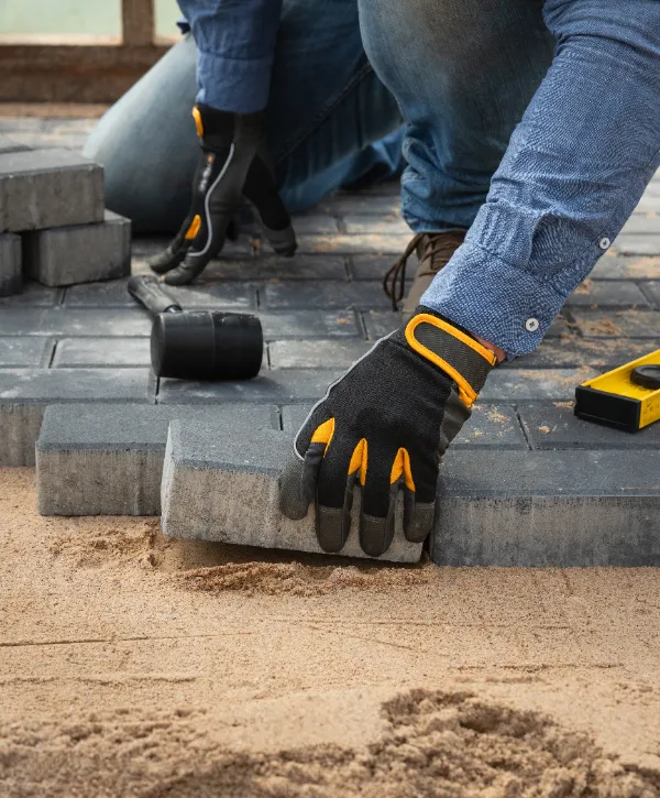 a worker installing concrete or stone pavers on a bed of sand for a driveway