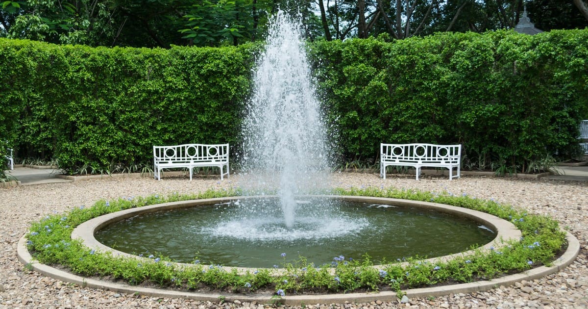 A high-pressure decorative water spray in a circular stone-edged garden pond, illustrating the visual differences of an aerator vs fountain for pond health and aesthetics.