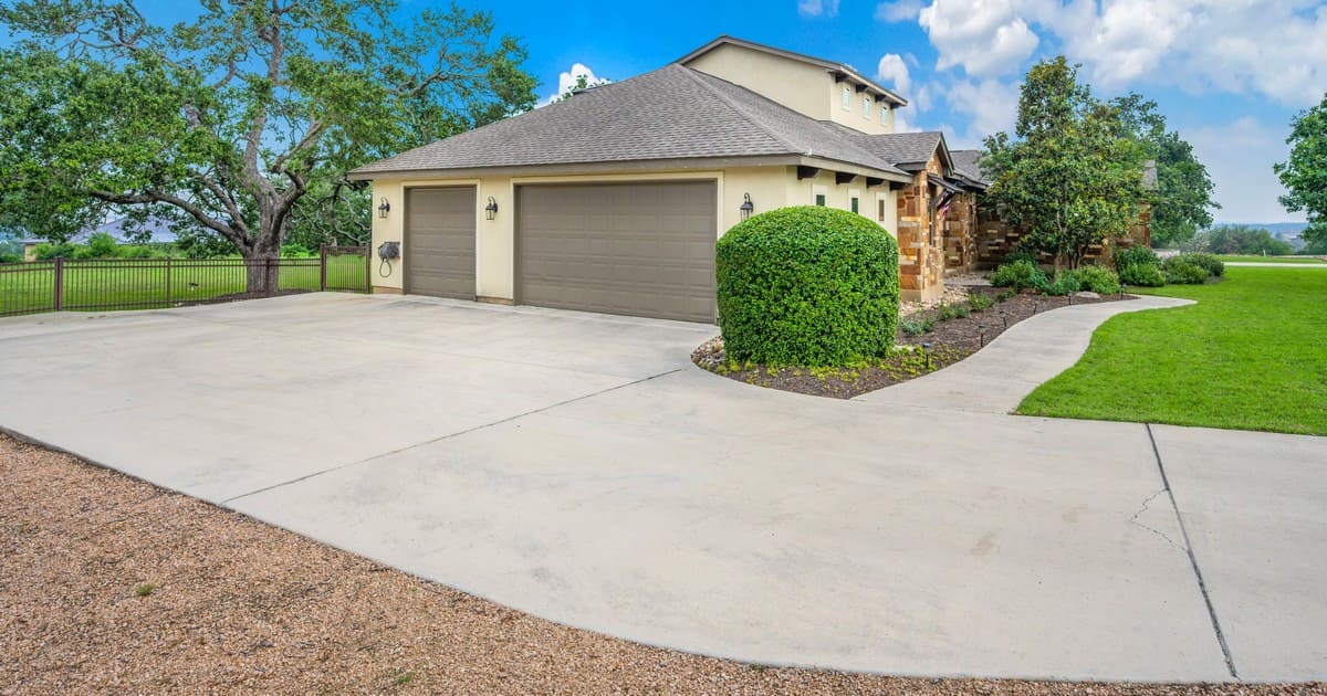 A spacious concrete driveway leading to a three-car garage of a suburban home, illustrating the clean look of a paver driveway vs concrete options.