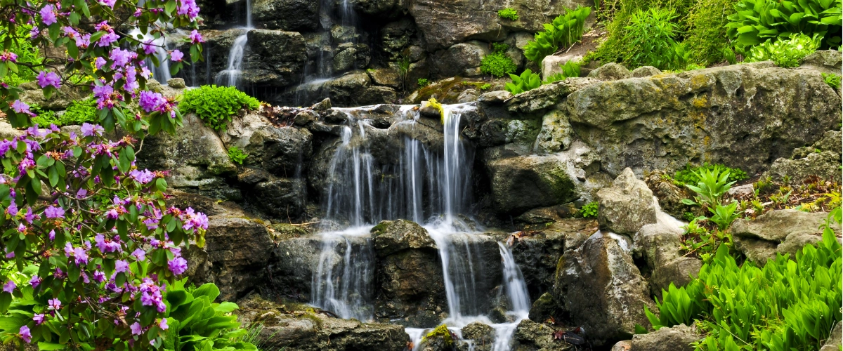 Multi-tiered pondless waterfall surrounded by lush plants and natural stone landscaping