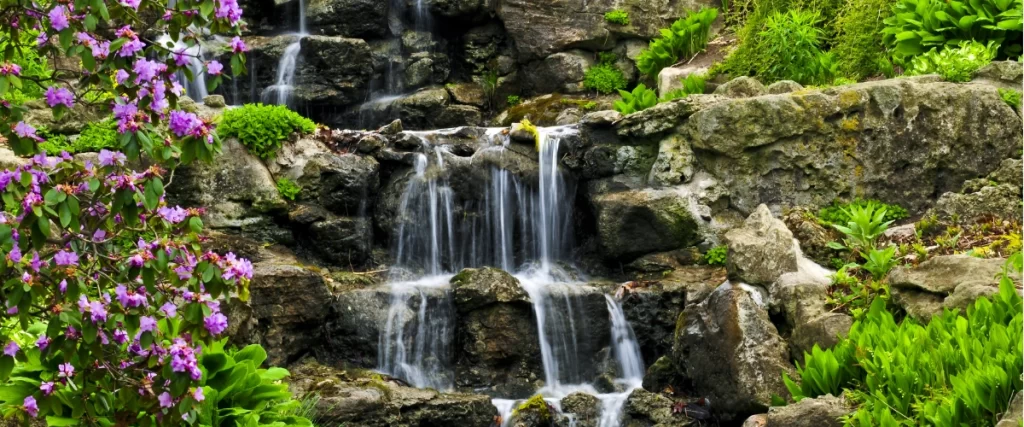 Multi-tiered pondless waterfall surrounded by lush plants and natural stone landscaping
