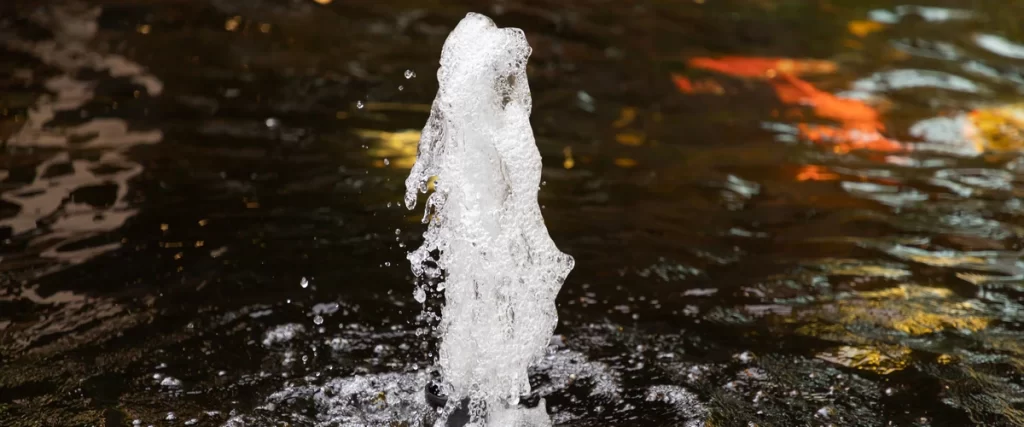 A close-up shot of a bubbling water fountain aerator in a pond to maintain high oxygen levels for fish.